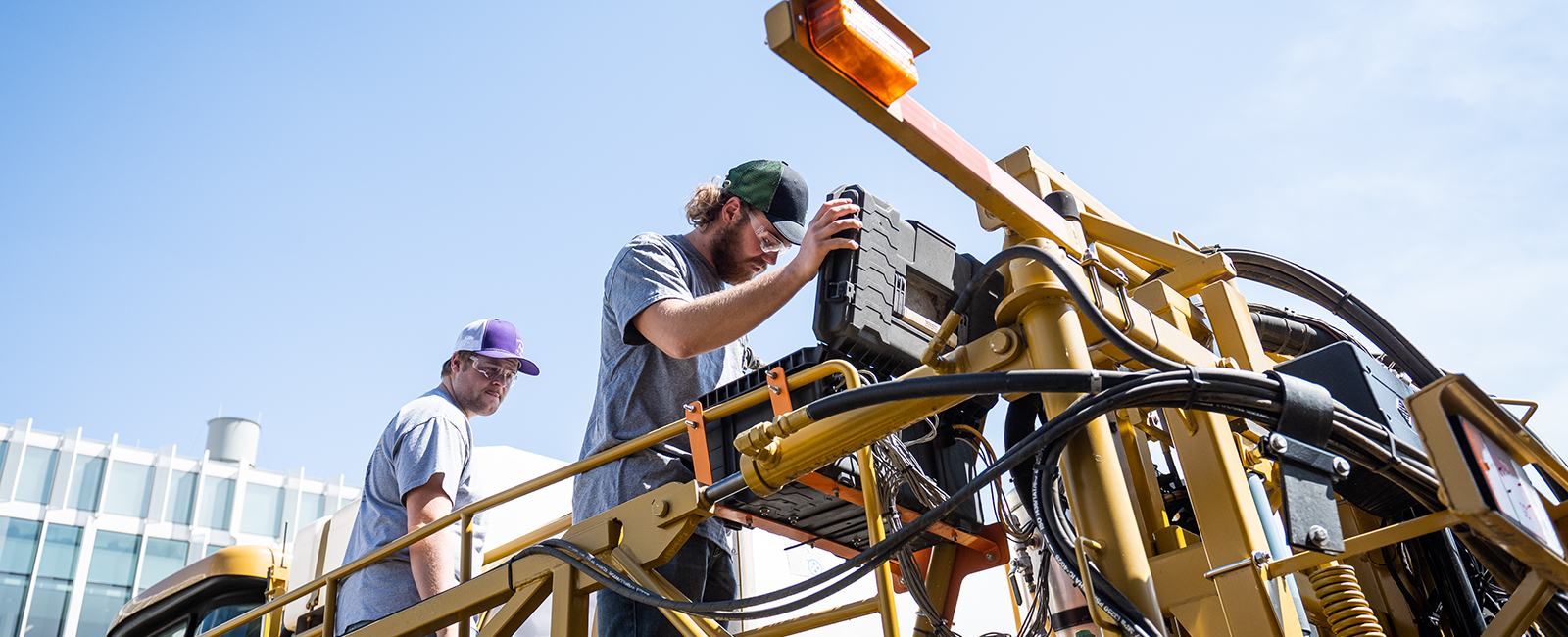 Two students work on large farming equipment.